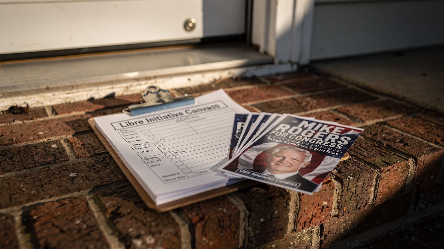 A clipboard of Libre Initiative canvass sheets and Mike Rogers flyers resting on a worn brick porch step in Holland, Michigan, a doorbell and storm door frame behind it, harsh late-afternoon sun rakin