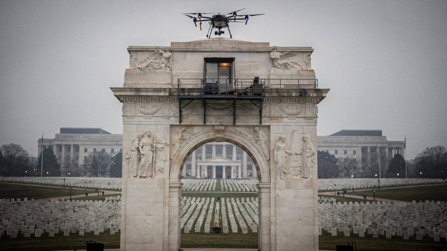A towering 250-foot triumphal arch of pale stone rising at Memorial Circle in Washington, D.C., a small military quadcopter drone perched on its upper cornice and a sniper observation platform mounted